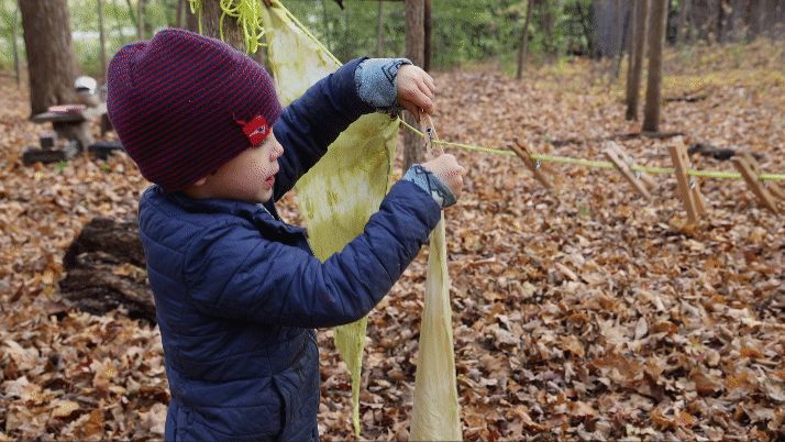 A small child clips tie dyed bandanas to an outdoor clothing line