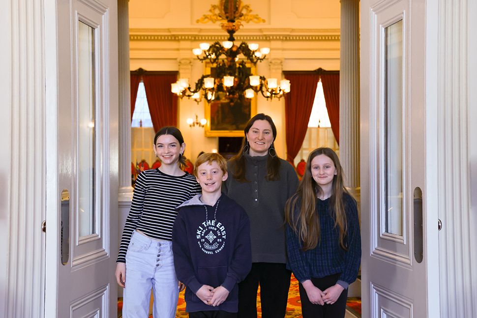 woman teacher standing with three middle school students in open doors to vermont statehouse testimony room in front of