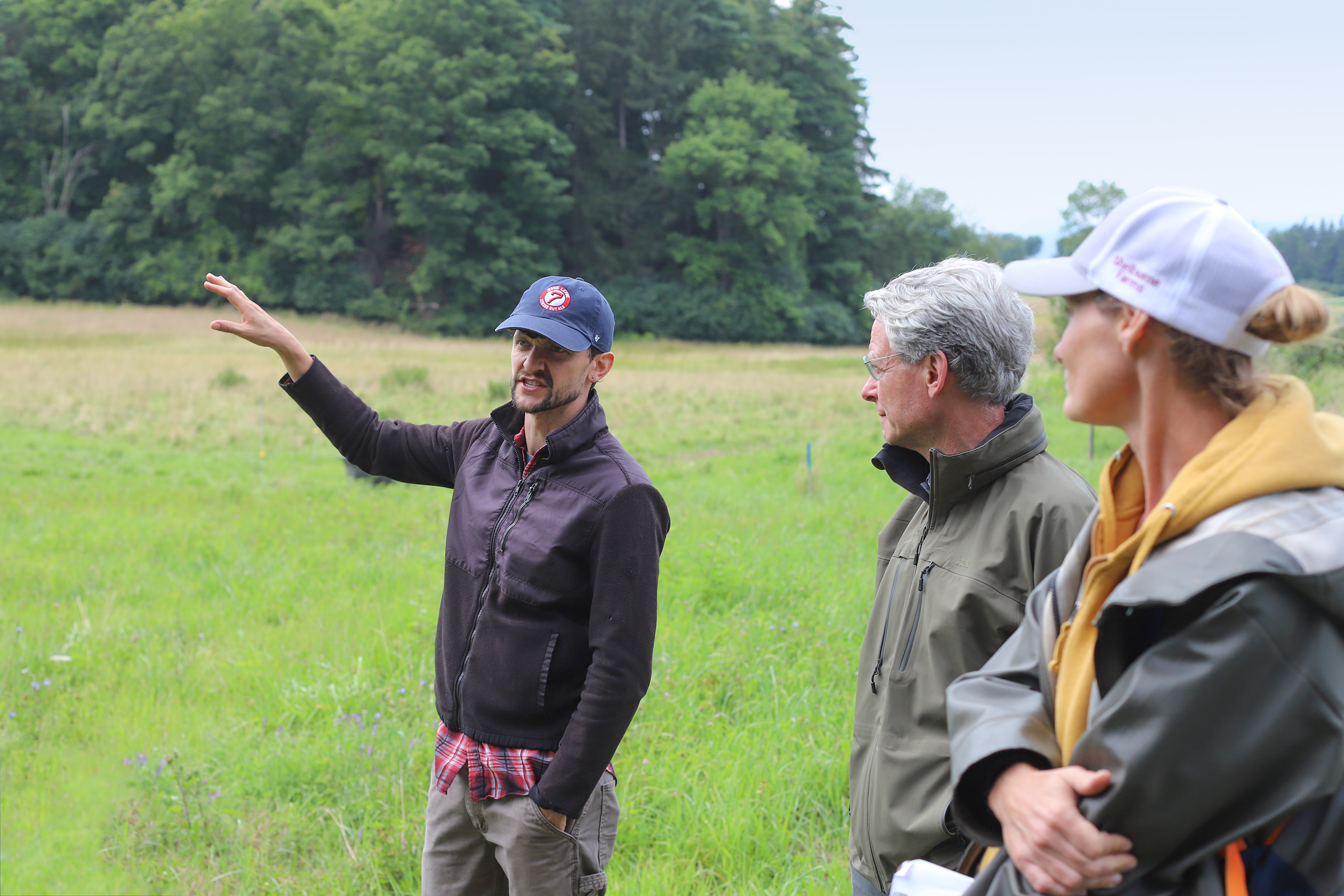 Man in a field gesturing and talking to several other people.