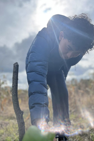 A high school student bends down to inspect a plant outdoors