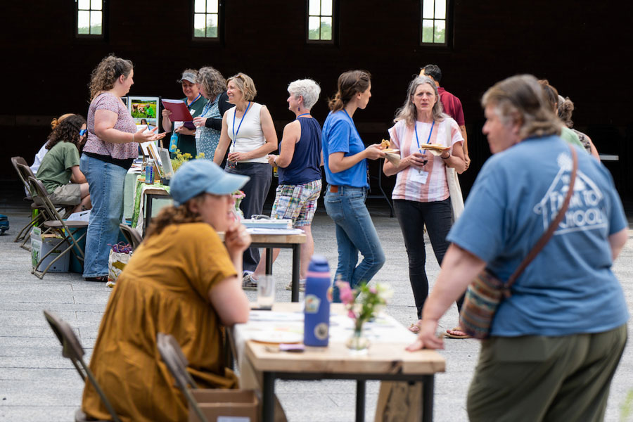 A group of people with various tables set up. Some are engaging in conversations, while others are seated at tables with informational materials.